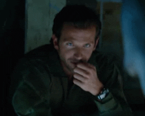 Celebrity gif. Bradley Cooper leans on a table and has his hand up to his lip. He looks at us flirtatiously and winks.