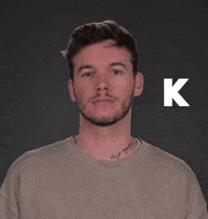 Celebrity gif. Dalton Fowler looks at us bored with a glitchy, white letter K next to him.