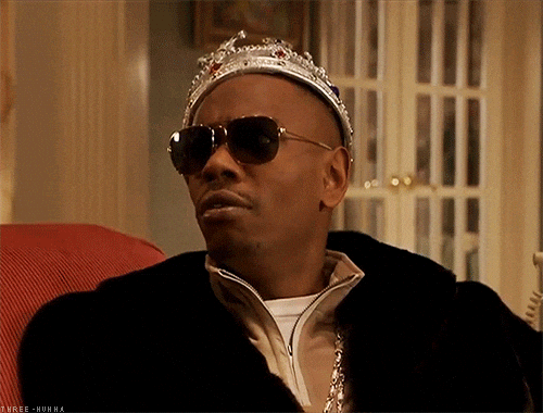 TV gif. A worried Dave Chappelle, wearing sunglasses and a crown, clutches stacks of money to his chest.