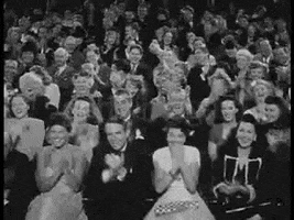 Video gif. Vintage-looking black and white footage of an audience dressed in suits and gowns clapping rapidly.