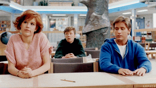 Movie gif. Sitting at tables in the library, Molly Ringwald as Claire, Emilio Esteves as Andrew, and Anthony Michael Hall as Brian in The Breakfast Club simultaneously shrug their shoulders.