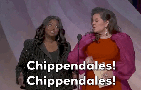 Oscars 2024 GIF. Melissa McCarthy and Octavia Spencer are introducing the award for Best Screenplay. Spencer gently circles her hips and moves her hands in the same motion while enthusiastically saying, "Chippendales! Chippendales!" McCarthy watches her, smiling, and holds a finger up.