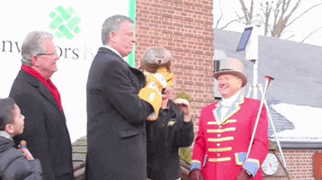 Political gif. Bill de Blasio is wearing big yellow gloves and holds a groundhog while grinning. He tries to hand the groundhog over to its keeper but the groundhog freaks out and launches itself out of his hands. 