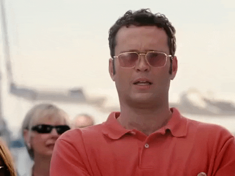 Movie gif. Vince Vaughn as Jeremy in "Wedding Crashers" wearing a salmon-colored polo and rose-colored glasses, stands with his arms crossed and raises his eyebrows in casual surprise.