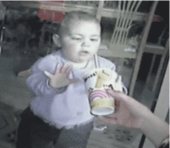 Video gif. A hand holds a drink with a straw to a window outside as a baby inside tries to drink it. 