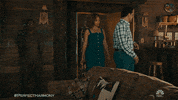 TV gif. TK as TK and Geno Segers as Dwayne in Perfect Harmony walk into a rustic-looking cabin, then turn around in fright when Rizwan Manji as Reverend Jax, dressed in treelike camouflage, jumps out from the wall and scares them. TK kicks Reverend Jax in the groin.
