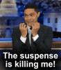 TV gif. Trevor Noah holds his bunched fists under his chin in excitement and says "The suspense is killing me!"