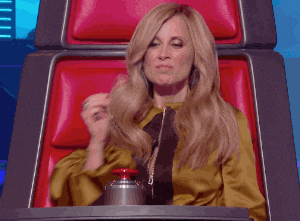 A woman sitting on a red chair in a TV show and pressing a red button with her left foot to turn the chair around.