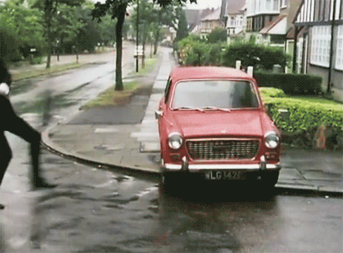 Video gif. Man runs up to a red car that’s parked on the sidewalk and hits it with a tree branch.