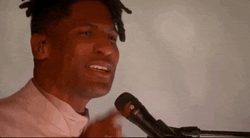 Oscars 2024 GIF. Close up shot of Jon Batiste performing "Never Went Away" from American Symphony. He points at someone in the audience as he sings a high note before looking down and smiling as he continues onto the next verse. 