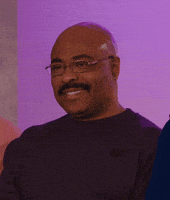Video gif. Man with glasses and a mustache smiles and looks around awkwardly.