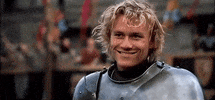 Movie gif. Heath Ledger as William in A Knight's Tale. He's wearing knights armor and gives us a disarming grin and a wink.