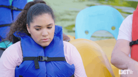Reality TV gif. Kennedy Owen from The Gary Owen Show sits somberly, wearing a life jacket inside of a boat.