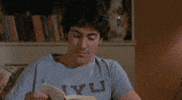 Video gif. Man is peacefully reading a book before he suddenly yells, "Jesus Christ!" He drops the book and falls to his knees, clawing at his face while screaming to the heavens, "Why!? God! Why!?," which appears as text. His anguish continues to escalate as he stands up and rips open his shirt.