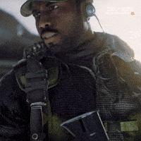 Sponsored gif. Man in combat gear slowly turns to look at a military helicopter where people are boarding.