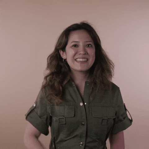 Reaction gif. A Disabled Vietnamese-American woman hemorrhagic stroke survivor with left-sided hemiplegia, brown sun-bleached hair styled in waves gives you a thumbs up, smiling broadly.