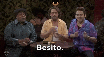 Video gif. Saturday Night Live castmember Mikey Day and guest host Ryan Gosling are dressed as Beavis and Butt-head for a sketch. Day and Gosling are sitting in the front row of a talk show audience. The two of them are staring straight ahead with goofy smiles on their faces. 