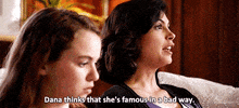 TV gif. Morena Baccarin as Jessica on Homeland sits on a white couch next to a girl in the foreground. She says glibly as the girl turns to look at her, "Dana thinks that she's famous in a bad way."