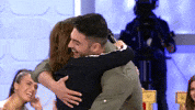 Video gif. Actor Toñi Moreno embraces a woman and picks her up in what appears to be a TV set with other people seated in chairs and watching on with big smiles. 