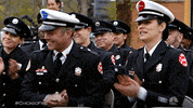 TV gif. Crowd of police officers in dress blues from One Chicago smile and clap enthusiastically.