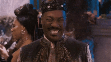Movie gif. Eddie Murphy as Prince Akeem in Coming to America 2 smiles a big toothy grin at the camera as he laughs. He points his finger and wags it as if knowing what he’s laughing at is bad. 