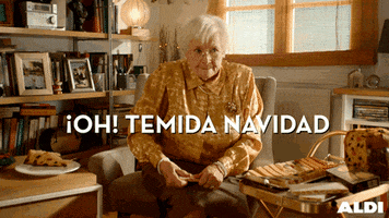 Ad gif. White-haired elderly woman sits in a chair next to a plate of fruitcake, struggling to break a slice in half over her knee. Text, in Spanish, reads "Oh! Temida Navidad."