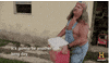 TV gif. An older man from Swamp People with long gray hair, wearing shirtless overalls and an American flag bandanna carries a red cooler out of a house. He speaks to us with a vague frown. Text, "It's gonna be another long day."