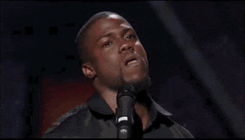 Celebrity gif. An annoyed Kevin Hart stands behind a microphone with head tilted to one side, tongue pushing against his bottom lip as his gaze shifts to the side. 