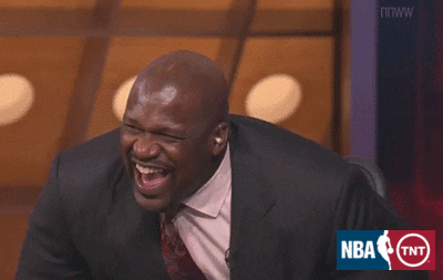 Sports gif. Wearing a dark gray suit jacket, Shaquille O'Neal leans forward in his seat for a prolonged, emphatic laugh.