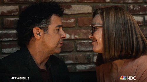 TV gif. Jon Huertas and Mandy Moore as Miguel and Rebecca in This Is Us kiss affectionately.