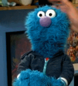 Video gif. Fluffy blue puppet resembling a Sesame Street character gets scratched on the head by a person out of frame; he looks over at the person.