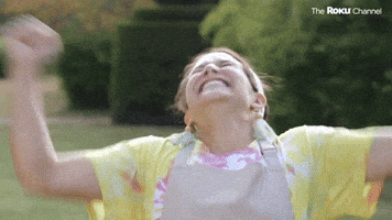 Reality TV gif. Talking head of a contestant on The Great American Baking Show, ecstatic, smiling broadly and shaking her arms in the air with speed and vigor.
