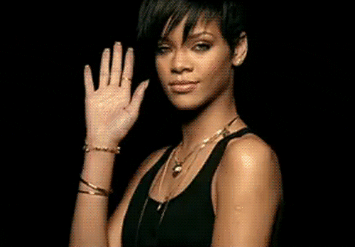 Celebrity gif. Rihanna looks fierce as she smiles at us with half lidded eyes and closed lips and waves.