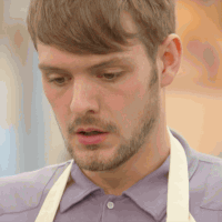 Reality TV gif. John Whaite from the Great British Bake Off exhales, blowing out his cheeks, appearing frustrated.