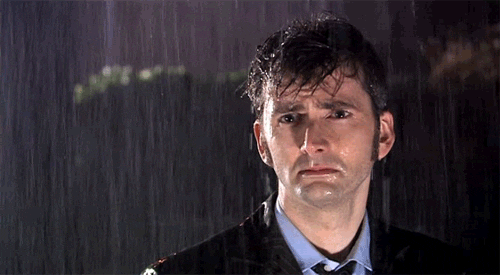 TV gif. David Tennant as The Doctor on Doctor Who stands in the pouring rain with a sad gaze. His hair and suit are soaked.