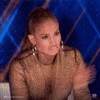 Reality TV gif. Jennifer Lopez as host of World of Dance wears a gold sequin turtleneck and a serious pout as she stands up to clap like she's impressed. 