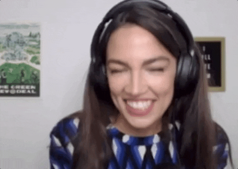 Political gif. Alexandria Ocasio-Cortez fans her face and throws her head back indicating heat before coming back towards the screen, smiling.