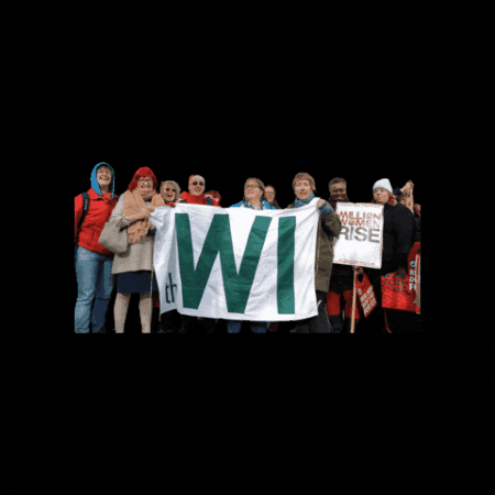 Photo gif. A group of women hold up a banner that reads, "WI" standing for Women's Institute, and the photo zooms in and out.