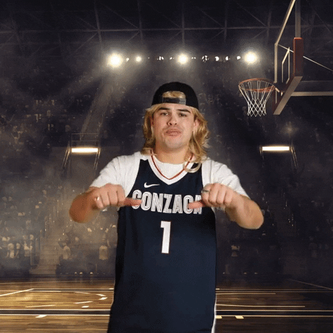 Video gif. Man wearing a Gonzaga basketball jersey gives us two thumbs down as he mouths an exaggerated, "Boo!" against a digitized background of a basketball court filled with stands. 