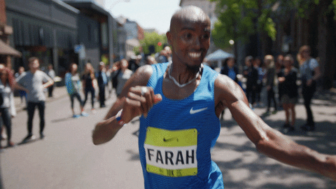 Sports gif. Mo Farah runs in a marathon. He grabs a bottled water from someone and takes a sip out of it. He then pours the rest of the water on his head and tosses it behind him, continuing to run down the street.