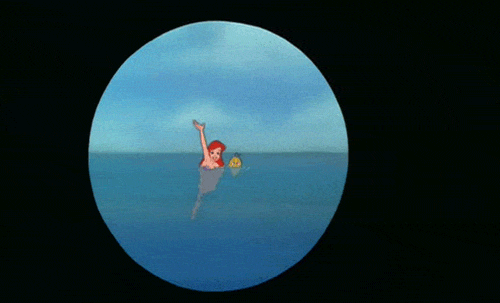 Movie gif. Ariel from The Little Mermaid is seen through a telescopic lens and she waves excitedly in the water, with Flounder floating happily next to her.