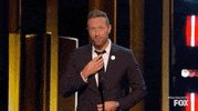 Celebrity gif. Chris Martin at I Heart Radio Music Awards adjusts his tie nervously, crosses his fingers, and says "fingers crossed."