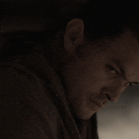 Movie gif. Jason Momoa as Duncan in Dune is close up in a dark room as he turns and looks off with an extremely serious gaze.