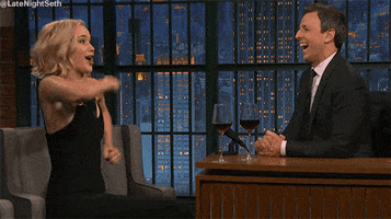 Late Night gif. Jennifer Lawrence is on the show and she imitates running by moving her arms swiftly at her side and makes a goofy face while Seth Meyers watches and laughs.