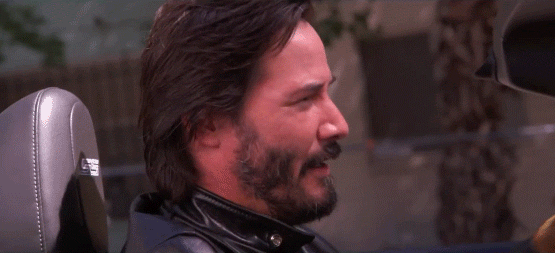 Celebrity gif. Keanu Reeves looks over his shoulder towards us and gives a dramatic wink. 