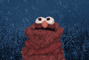 Sesame Street gif. Elmo shivers in the cold as snow falls around him and snow tipped trees are in the frosty background.