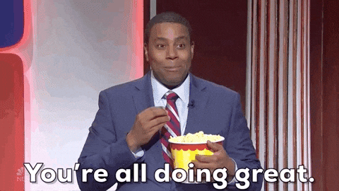 SNL gif. Wearing a dark blue suit, a smiling Kenan Thompson speaks to us as he snacks from a bucket of popcorn. Text, "You're all doing great."