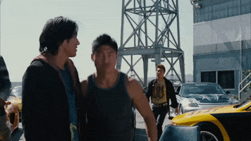 Movie gif. Sun Kang as Han Lue from the Fast and the Furious walking briskly past people on his way to punch someone in the face.