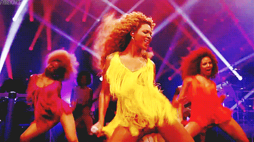 Music video gif. From the video for "End of Time," Beyonce dances in coordination with two other dancers on either side of her on stage filled with flashing lights.