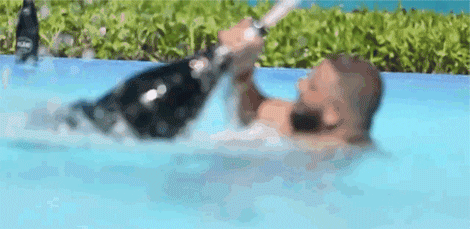 Celebrity gif. DJ Khaled in a swimming pool wrestling with a bottle of champagne half his size, which explodes in an arc over his head.